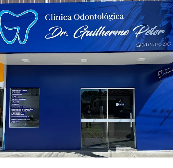 Fachada azul da Clínica Odontológica Dr. Guilherme Peter, com o letreiro do nome e do logotipo acima da porta de vidro da entrada
