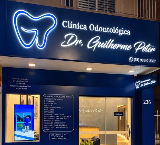 Fachada da Clínica Odontológica Dr. Guilherme Peter à noite, com o letreiro iluminado acima da porta de vidro